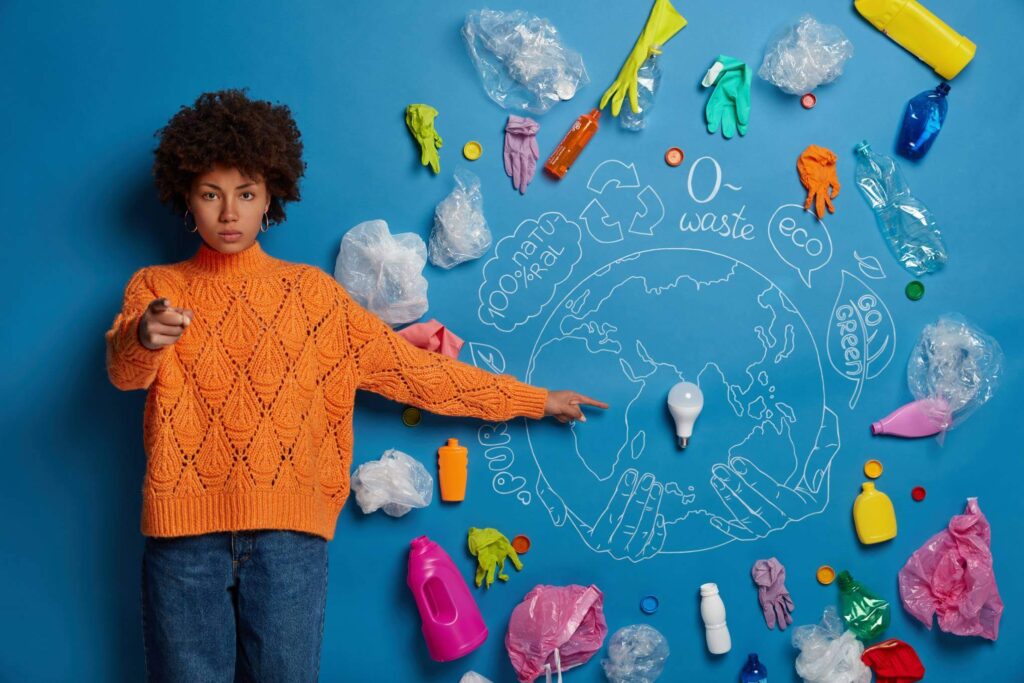 You are responsible for our planet. Serious Afro American woman explains problem of pollution points at drawn Earth with lightbulb much plastic litter indicates at camera asks to stop throwing garbage